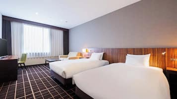 A hotel room with two beds, a desk, a chair, a TV, and a large window with curtains.
