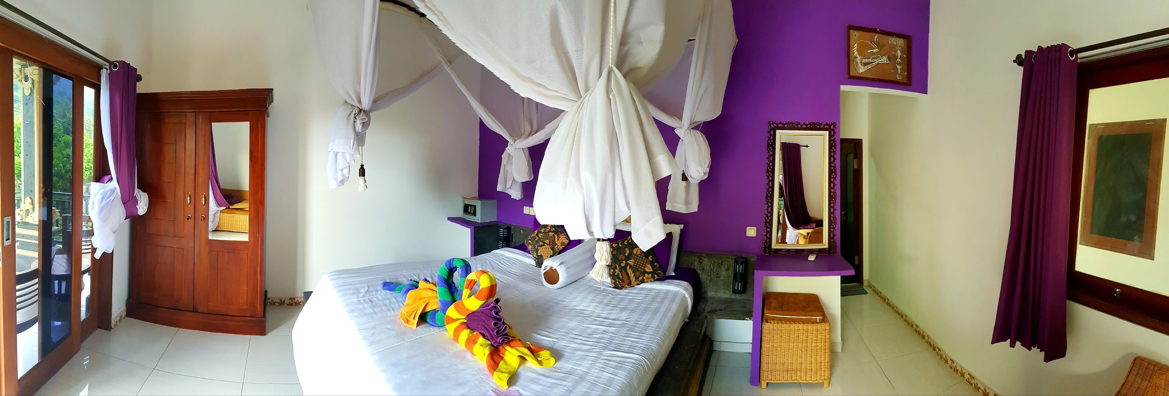 A room with a bed, a wooden door, a purple wall, and a mirror.