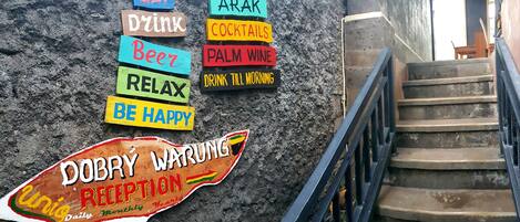Un mur orné d’enseignes colorées faisant la publicité de diverses boissons et une pancarte indiquant l’entrée du « Dobrý Warung ».