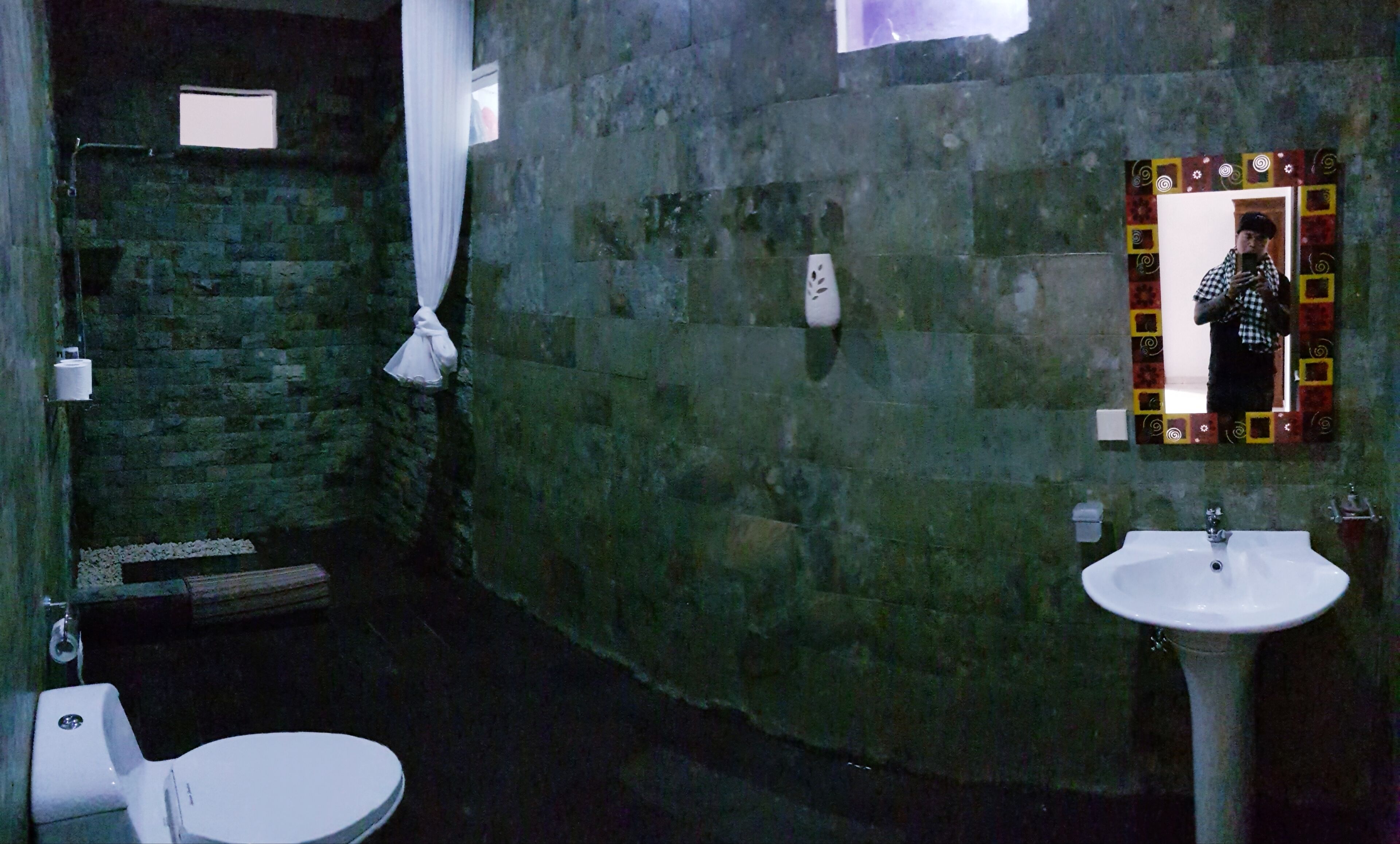Un baño con pared de piedra, un lavamanos blanco y un inodoro.