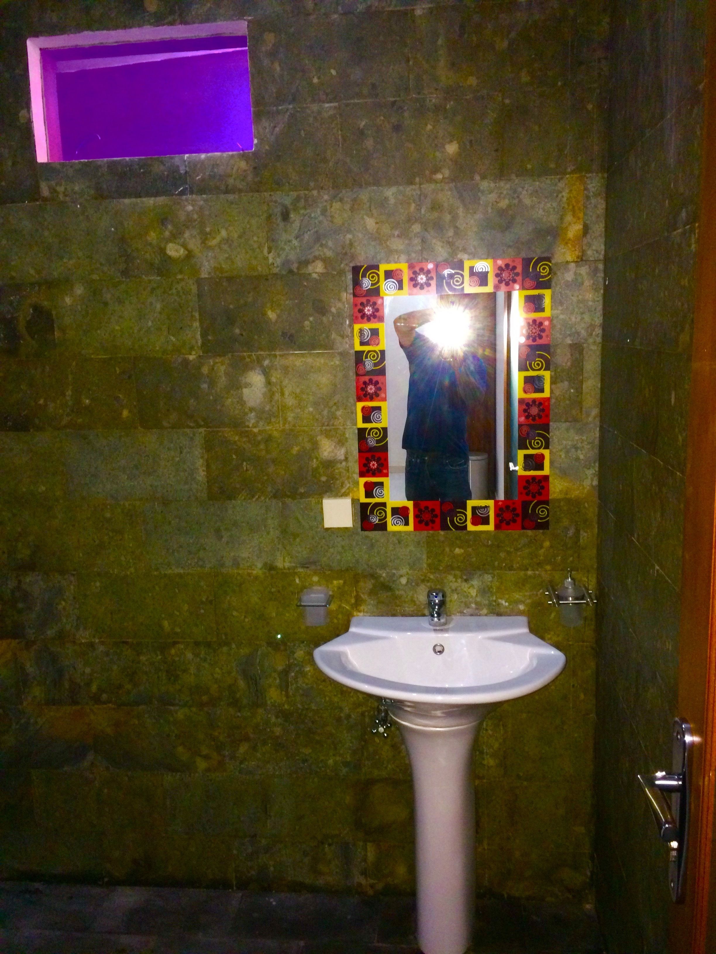 A bathroom with a white sink, a mirror with a colorful frame, and a stone wall.