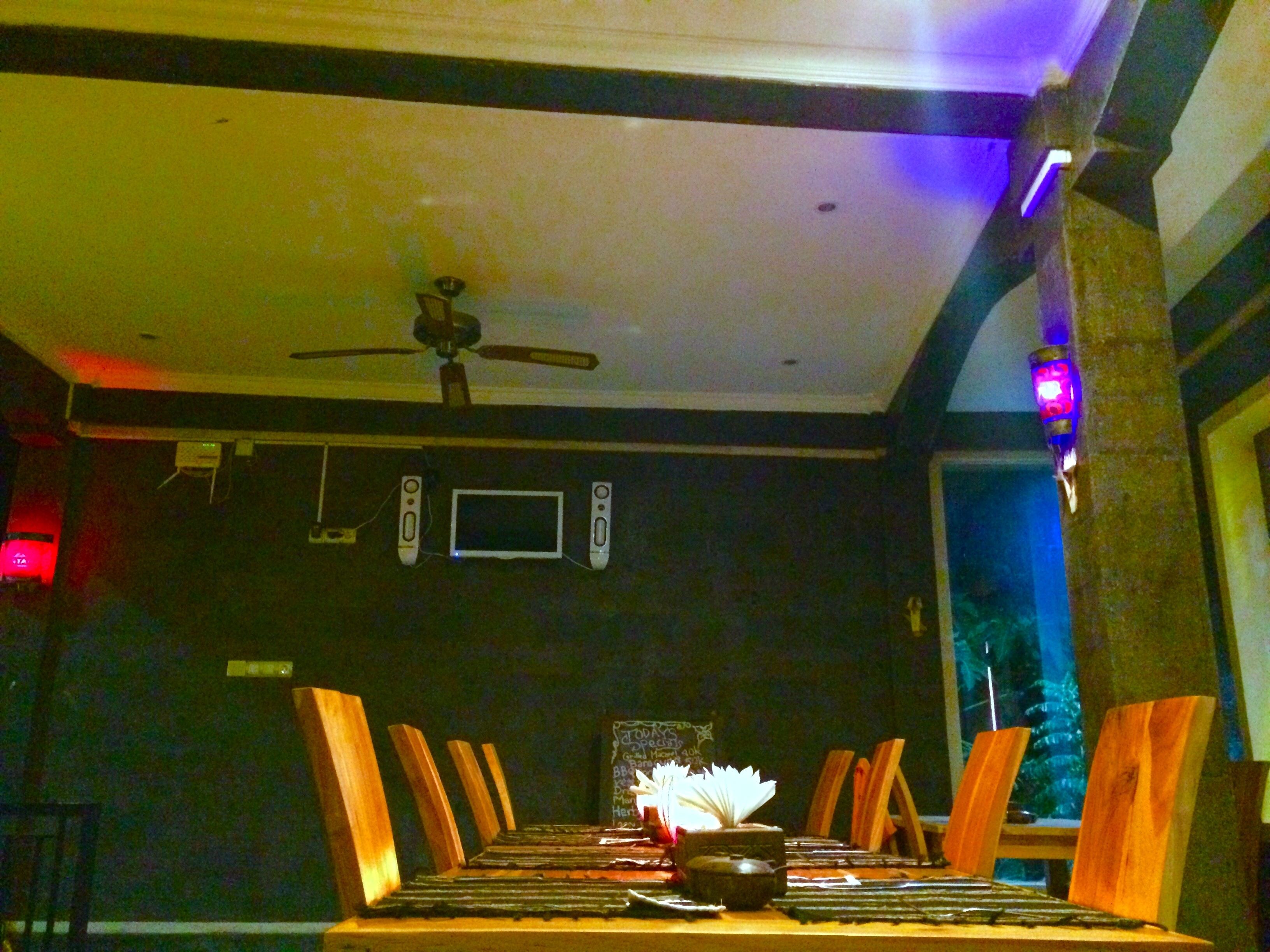 Un coin repas avec une table dressée pour deux personnes, un ventilateur de plafond et un téléviseur fixé au mur.