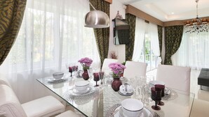 A modern dining area with a glass table set for a meal, surrounded by white chairs. - Leelawadee Pool Villa (Sattahip)