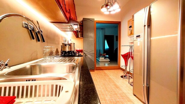 A modern kitchen with stainless steel appliances, a double sink, and a red accent chair. - Leelawadee Pool Villa (Sattahip)