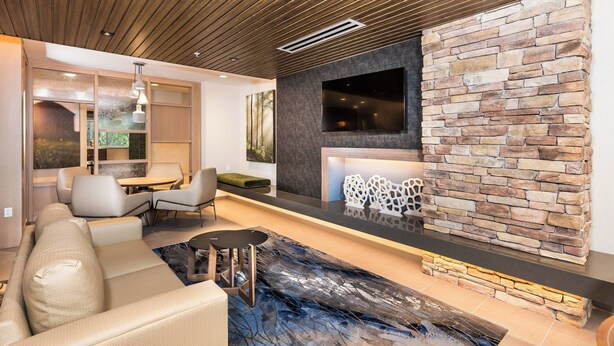 A modern living room with a stone fireplace, a sofa, a dining area, and a large abstract rug.