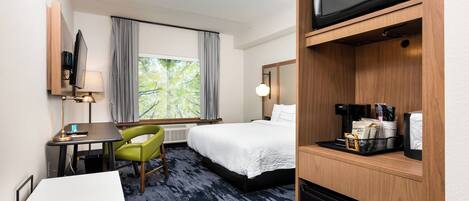 Habitación de hotel con cama, escritorio con silla, microondas, cafetera y ventana con cortinas.