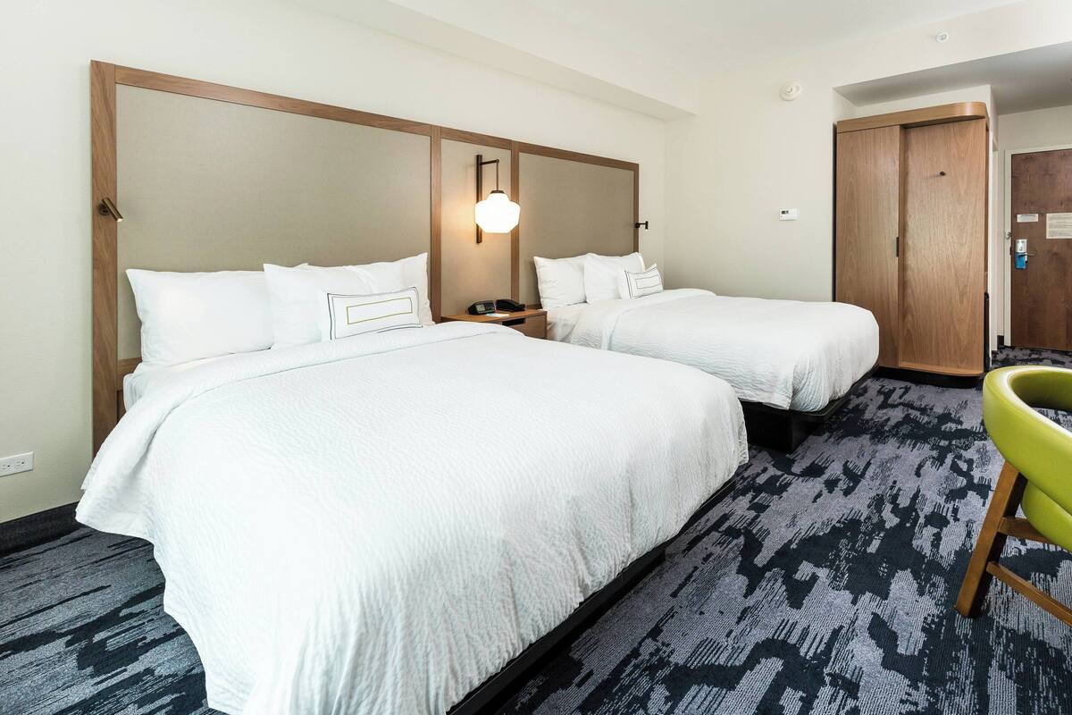 A hotel room with two beds, a wooden wardrobe, a desk with a phone, and a patterned carpet.
