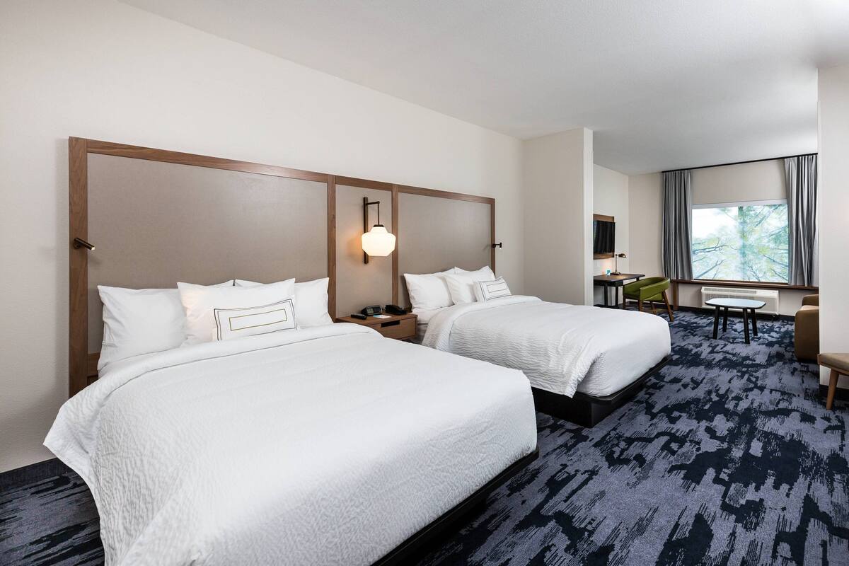A hotel room with two beds, a desk, a chair, and a large window with curtains.