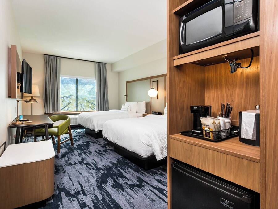 A hotel room with two beds, a desk with a chair, a TV, a microwave, and a coffee maker.