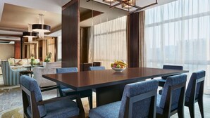 A modern hotel dining area with a large wooden table, blue upholstered chairs, and a bowl of fruit on the table.