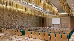A conference room with rows of chairs, a stage, and a large screen.