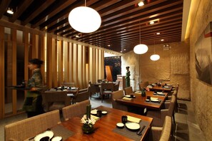 Un restaurante con paredes de madera, lámparas colgantes redondas y una pared de piedra. Las mesas están preparadas con platos, palillos y cuencos.