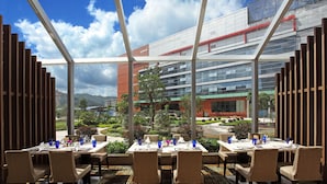 A restaurant with tables set for dining, a view of a modern building, and a landscaped garden.