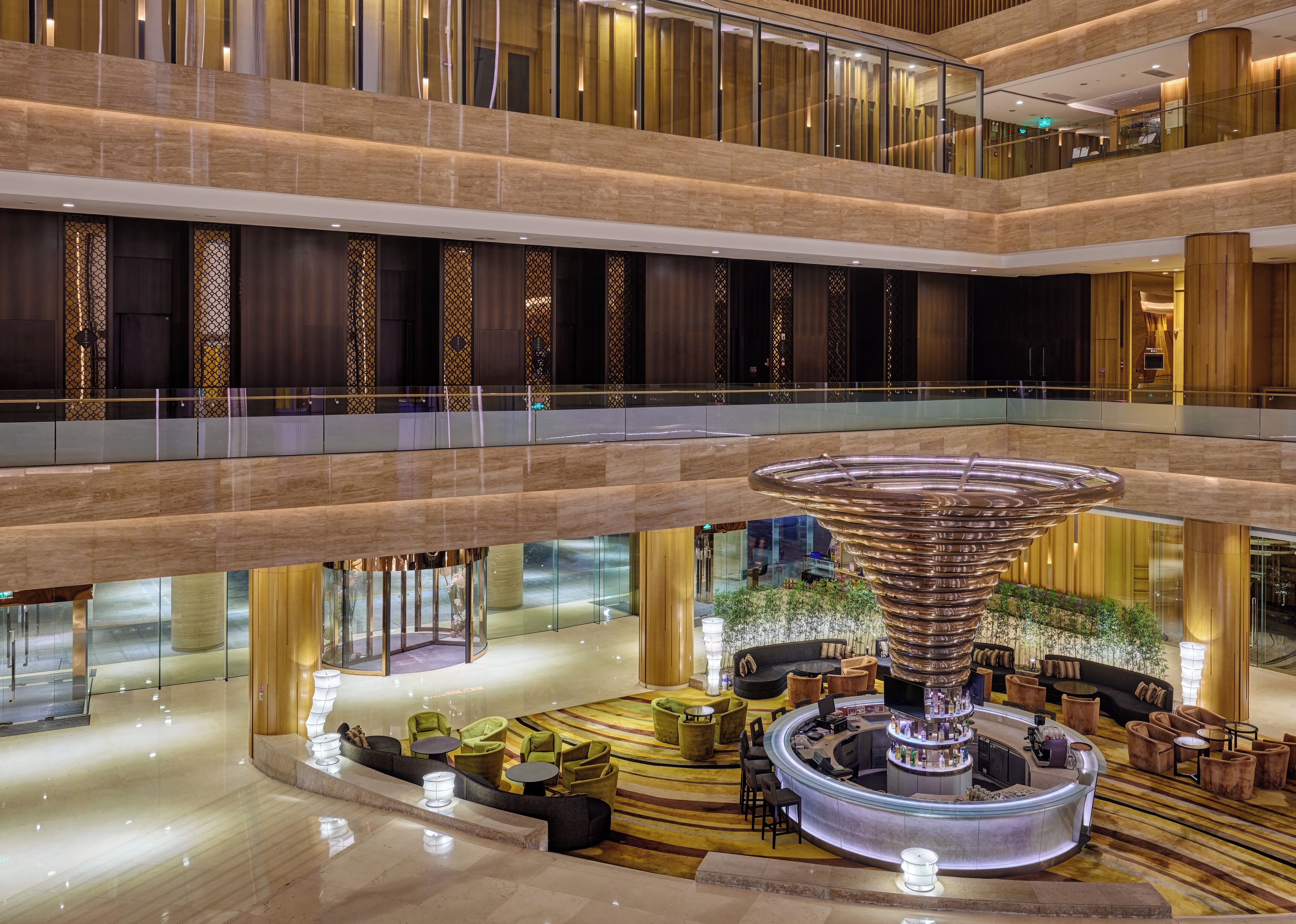 A multi-level hotel lobby with a central circular bar area, seating arrangements, and a decorative water feature.