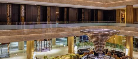 A multi-level hotel lobby with a central circular bar area, seating arrangements, and a decorative water feature.