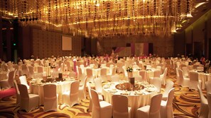 Un salón de banquetes con mesas redondas cubiertas con manteles blancos, sillas blancas y un techo decorativo.