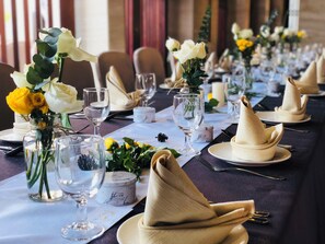 Une longue table à manger, dressée avec des serviettes blanches, de la vaisselle transparente et des centres de table floraux.