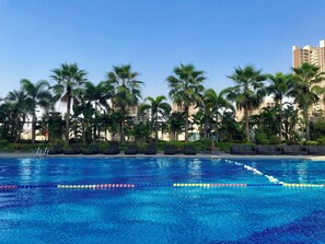 A swimming pool with clear blue water, surrounded by palm trees and lounge chairs. - Crowne Plaza Zhongshan Wing on City (Zhongshan)