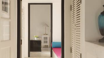 A hallway with a white door, a black cabinet, a small white table with a lamp, and a blue bed.