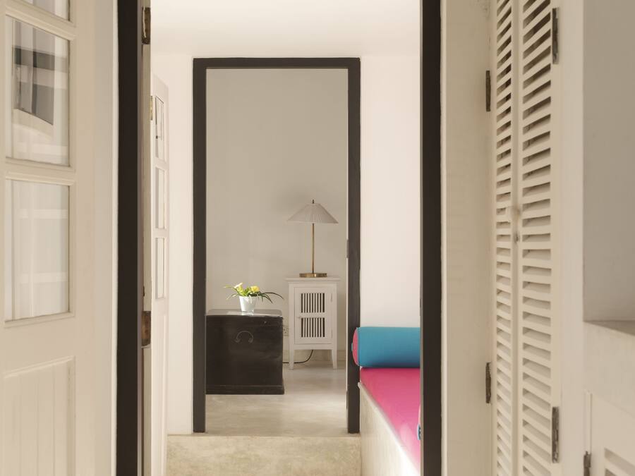 A hallway with a white door, a black cabinet, a small white table with a lamp, and a blue bed.