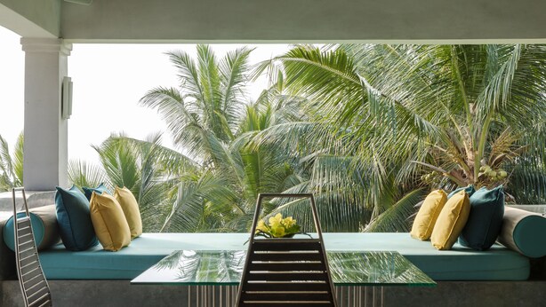 A modern outdoor seating area with a glass table, cushioned seating, and a view of palm trees. - Coco Tangalla (Tangalle)