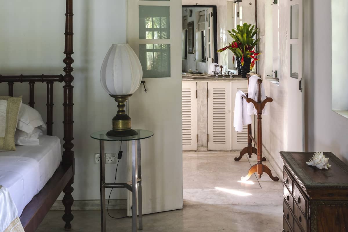 Quarto com cama de dossel, mesa de cabeceira com abajur e cômoda.