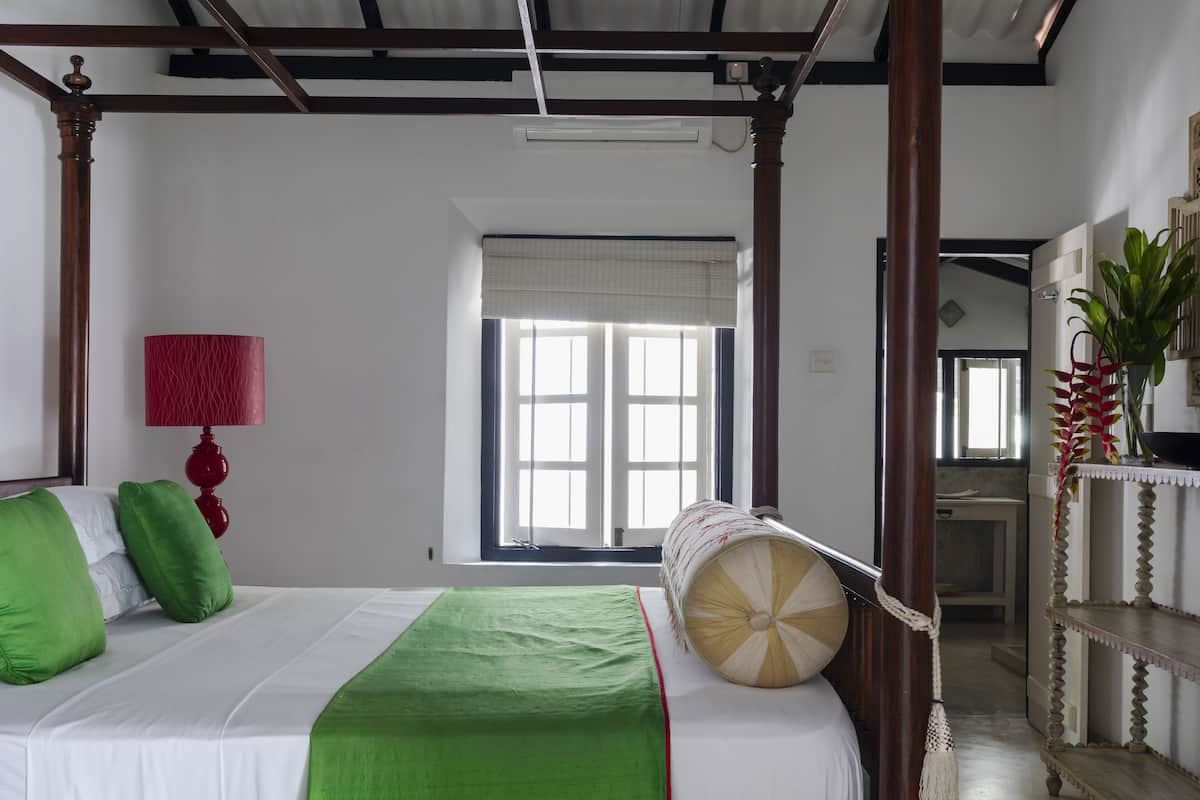 Quarto com uma cama de dossel, um abajur vermelho e uma janela grande com persianas.