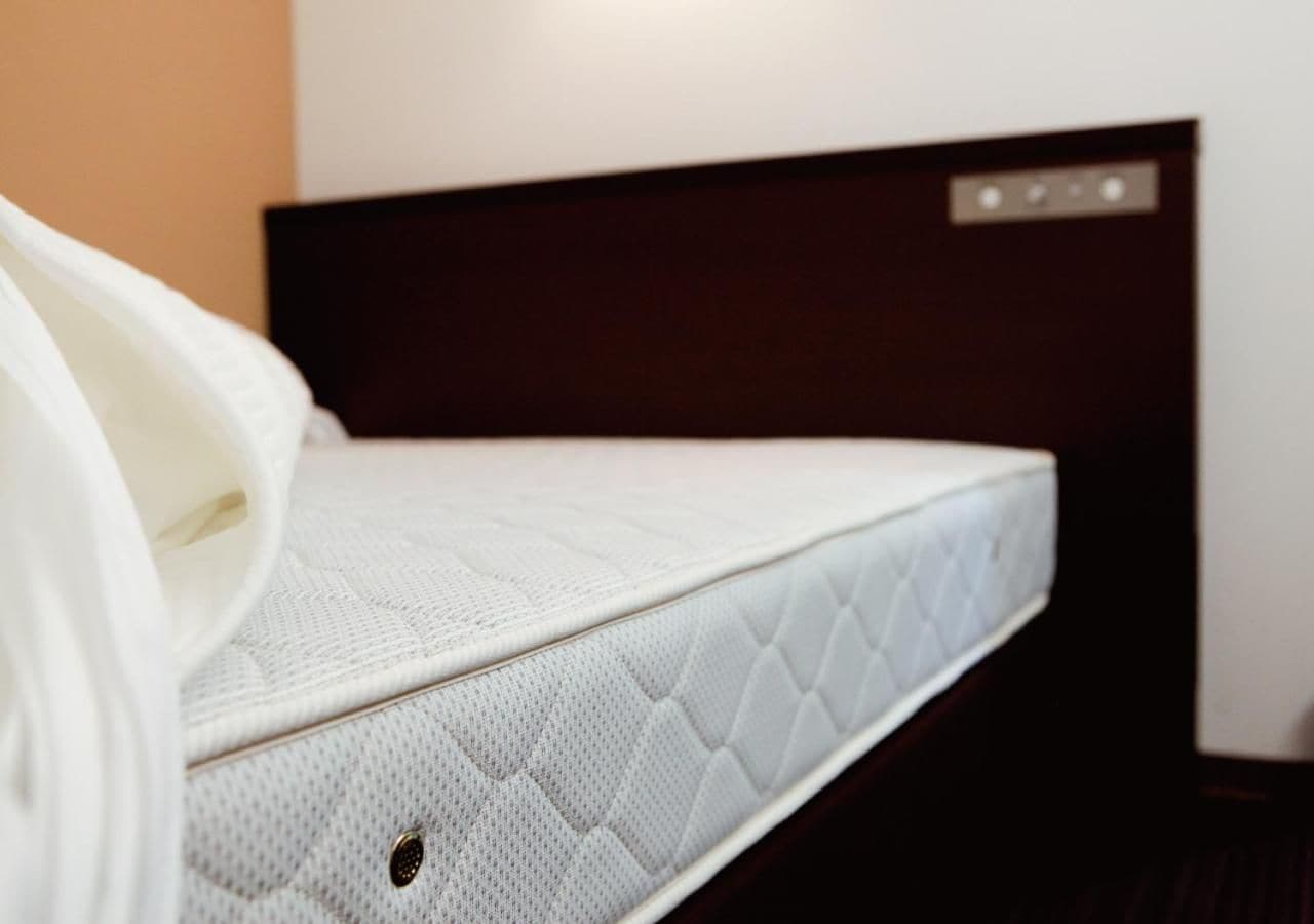 En enkeltseng med hvid madras og mørkt sengegærde i et hotelværelse.