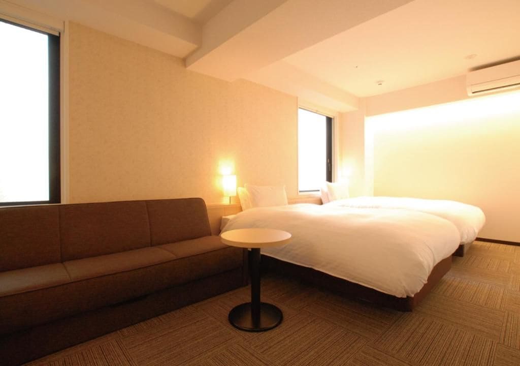 A hotel room with a bed, a sofa, a small round table, and two bedside lamps.