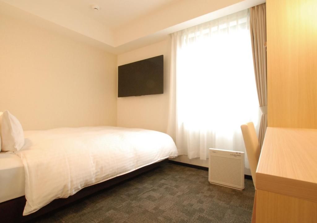 Quarto de hotel com cama, televisão de tela plana na parede, janela com cortinas e radiador.