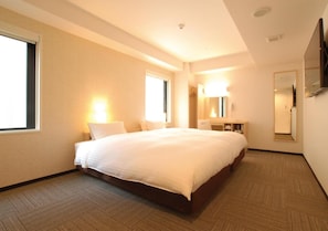 Una habitación de hotel con una cama grande, un escritorio, un espejo y una ventana.