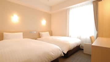 A hotel room with two beds, a desk, and a window with curtains.