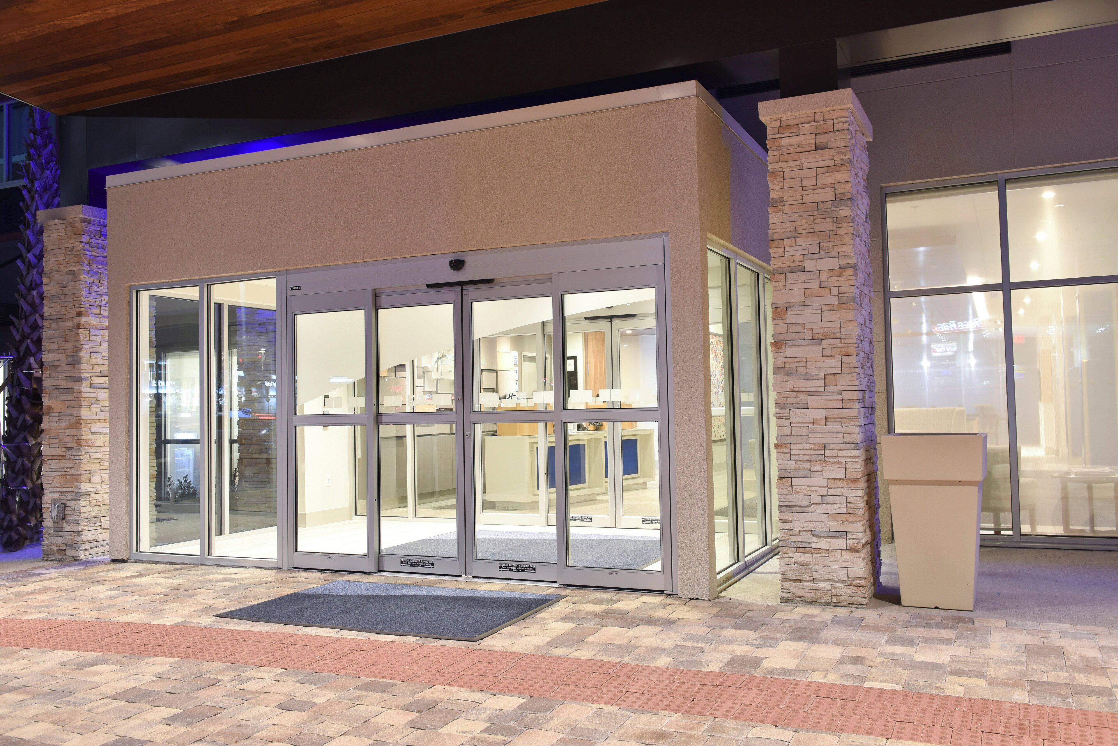 L’entrée d’un hôtel, avec une porte en verre, une façade en pierre et un espace d’entrée pavé.