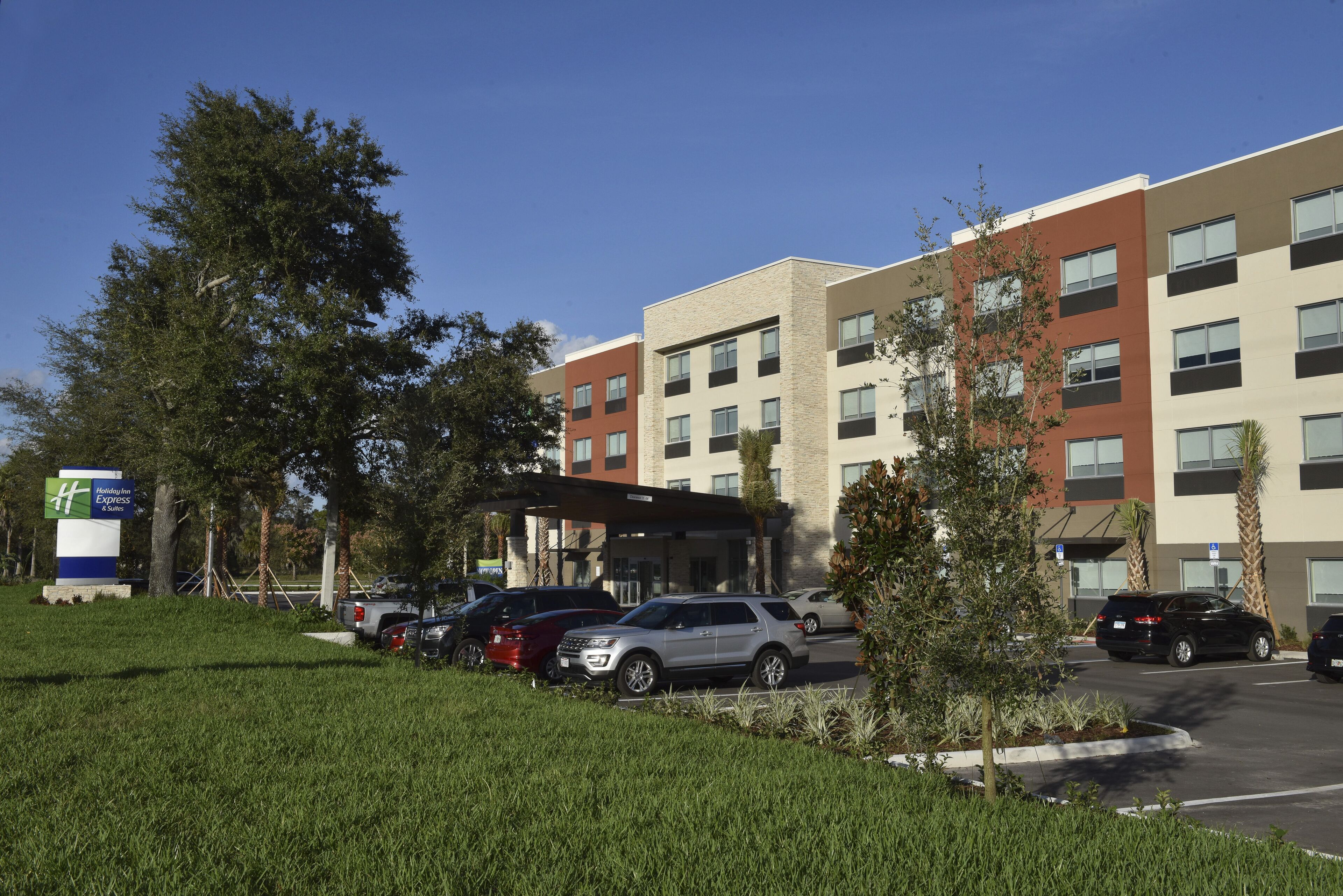 A hotel with multiple floors, a parking lot with several cars, and a sign for the hotel.