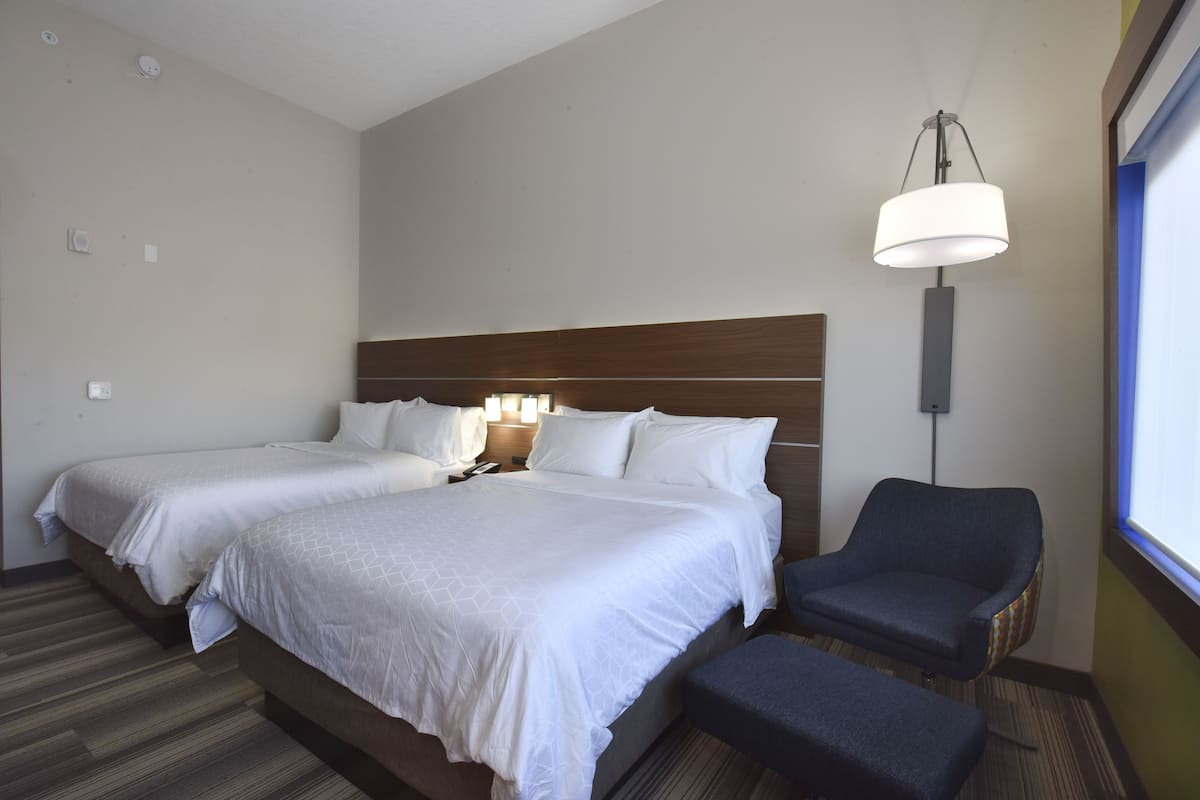 Une chambre d’hôtel avec deux lits, un bureau, une chaise et une grande fenêtre.