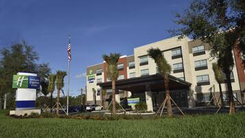A Holiday Inn Express & Suites building with a 'NOW OPEN' sign, surrounded by palm trees and a clear blue sky.