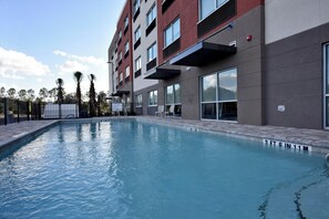 Une piscine dont la profondeur est indiquée par des repères, entourée d’un bâtiment à plusieurs étages doté de grandes fenêtres.