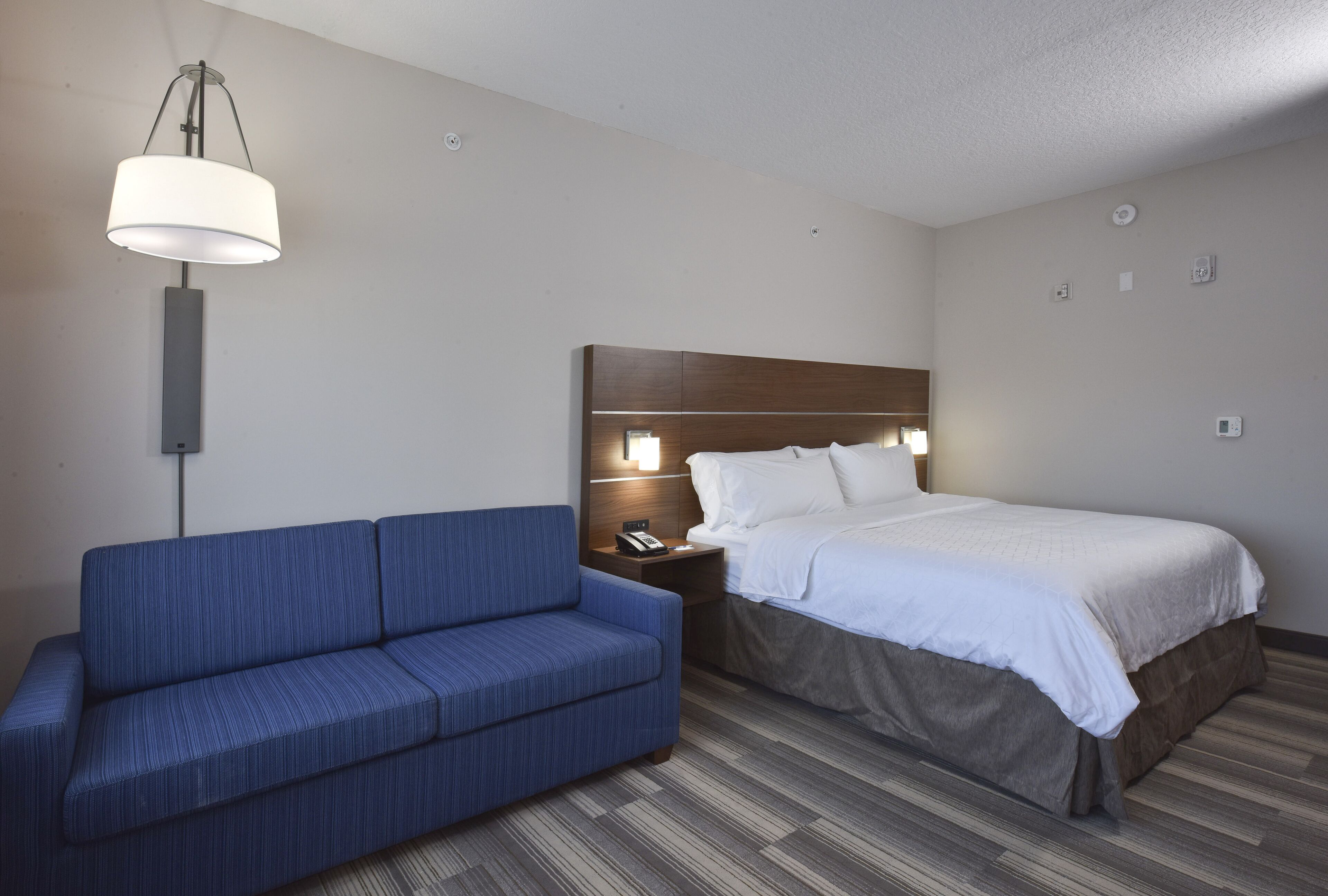Een hotelkamer met een bed, een blauwe bank, een nachtkastje met een lamp en een wandlamp.