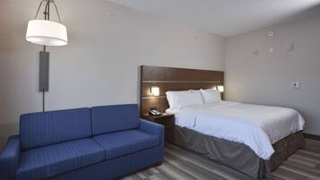 Een hotelkamer met een bed, een blauwe bank, een nachtkastje met een lamp en een wandlamp.