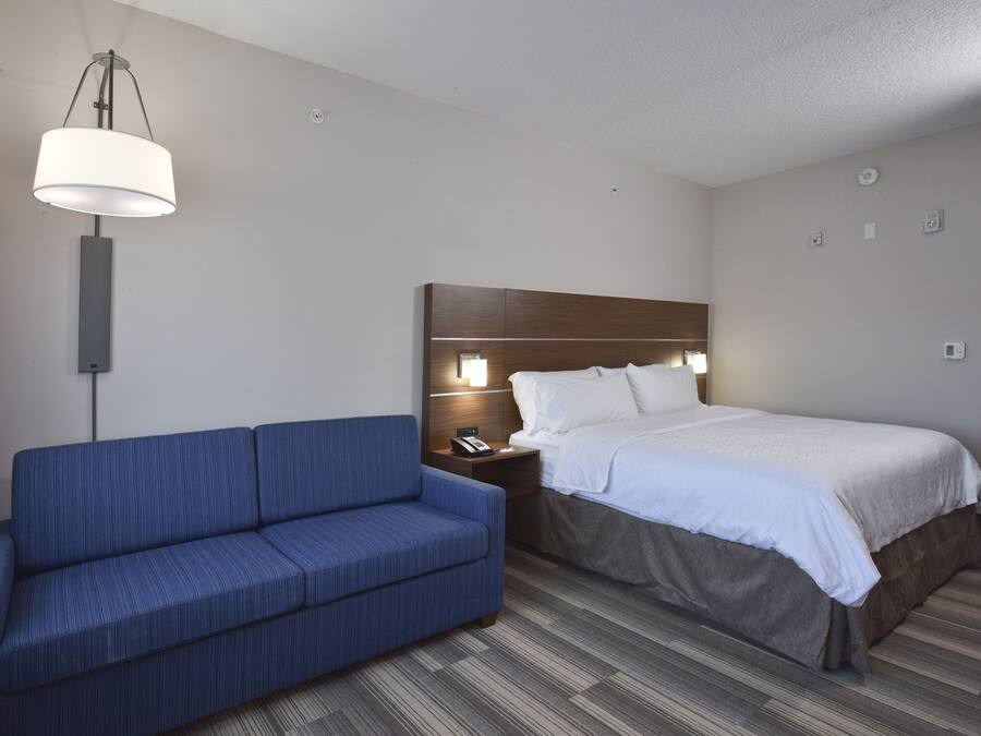 Een hotelkamer met een bed, een blauwe bank, een nachtkastje met een lamp en een wandlamp.