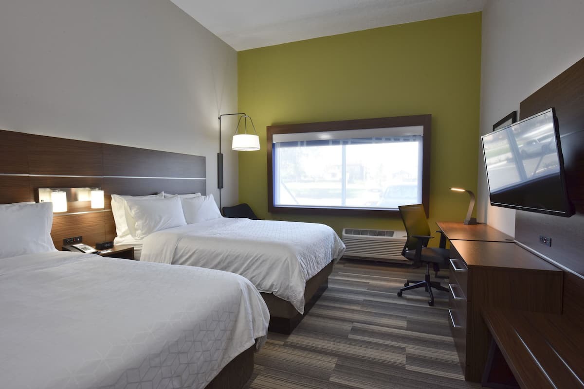 Une chambre d’hôtel avec deux lits, un bureau avec une télévision, une lampe et une fenêtre donnant sur l’extérieur.