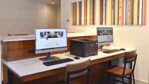 Ein Hotelrezeptionstresen mit zwei Computermonitoren, einem Samsung-Desktop-Computer, einer Tastatur, einer Maus und zwei Holzstühlen.