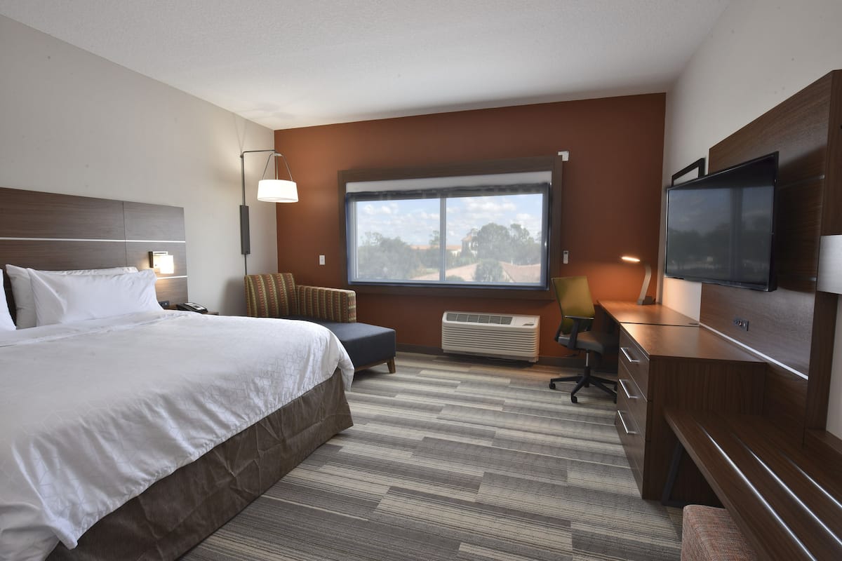 Une chambre d’hôtel avec un grand lit, un bureau, une chaise, une télévision et une fenêtre donnant sur l’extérieur.