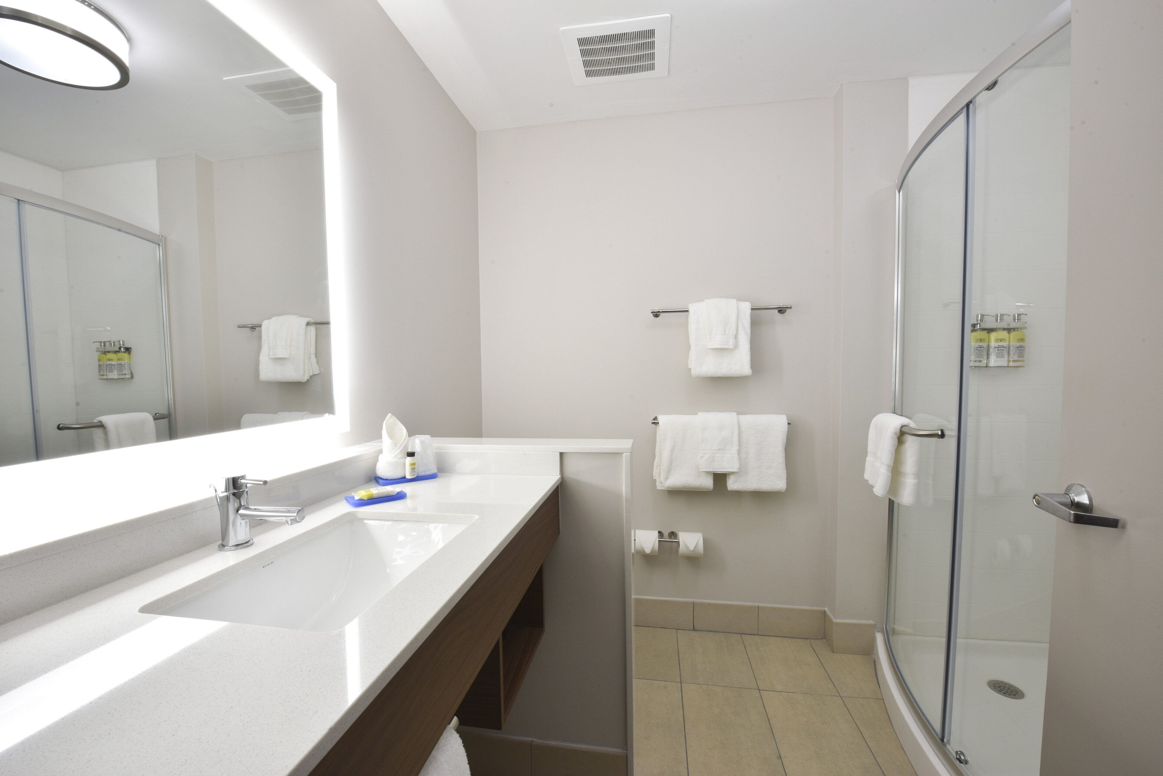 A modern bathroom with a large mirror, two sinks, a shower, and a toilet.