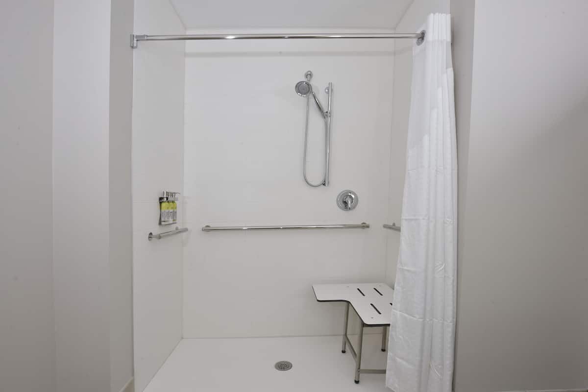 Une douche à l’italienne équipée d’une barre d’appui, d’un pommeau de douche amovible et d’un rideau blanc.