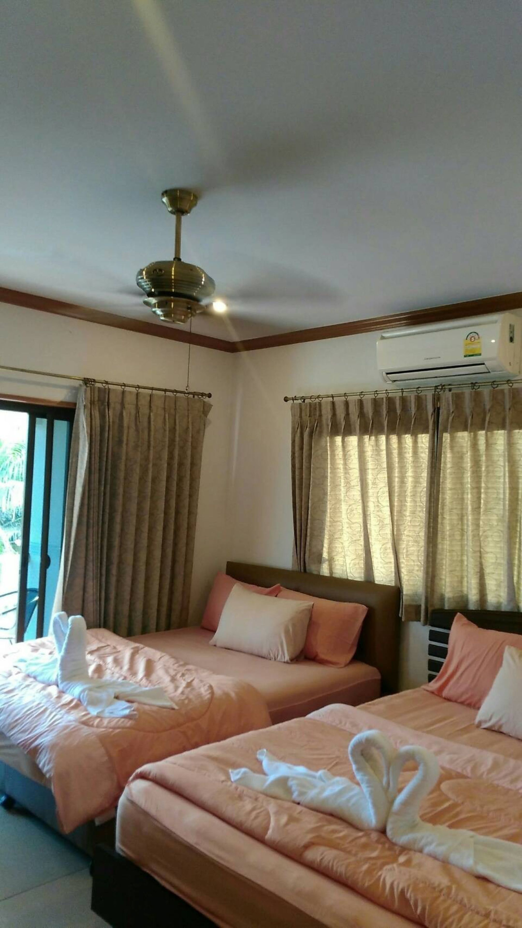 Ein Hotelzimmer mit zwei Betten, einem Deckenventilator, einer Klimaanlage und Vorhängen.