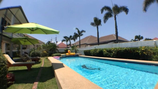 A swimming pool with lounge chairs and umbrellas, surrounded by palm trees and a well-maintained lawn. - Baan TonPalm Pool Villa Huahin (Hua Hin)
