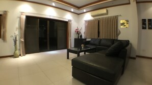 A modern living room with a black leather sofa, a glass coffee table, and a sliding glass door leading to a balcony. - Baan TonPalm Pool Villa Huahin (Hua Hin)