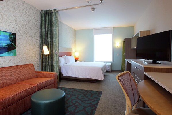 A hotel room with a bed, a sofa, a desk, a chair, a television, and a window. - Home2 Suites by Hilton Nampa (Nampa)