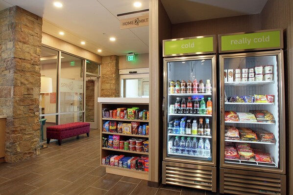 A hotel lobby with a stone wall, a red bench, and two refrigerated display cases labeled "cold" and "really cold" with various beverages and snacks.
